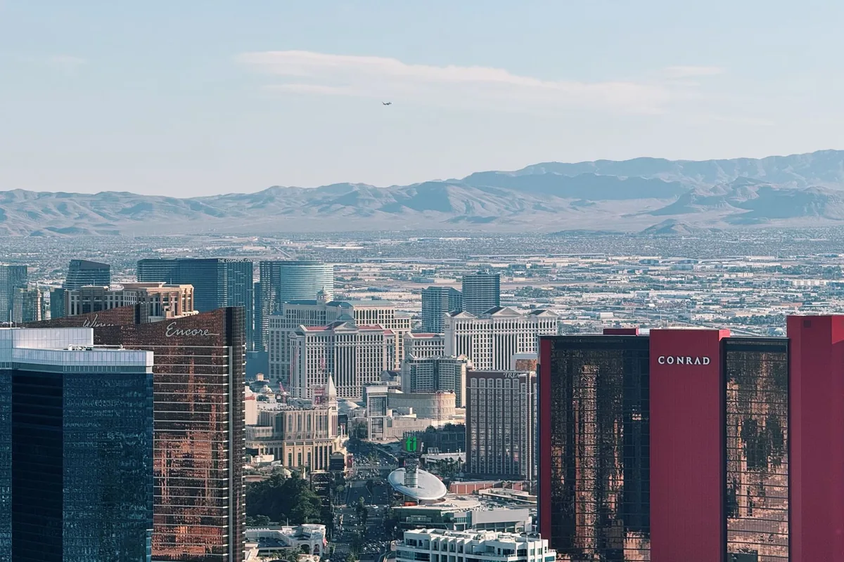 Resort towers along the Las Vegas Strip in the foreground, with the low sprawl of the valley behind them and a long bare mountain range across the horizon under a clear sky