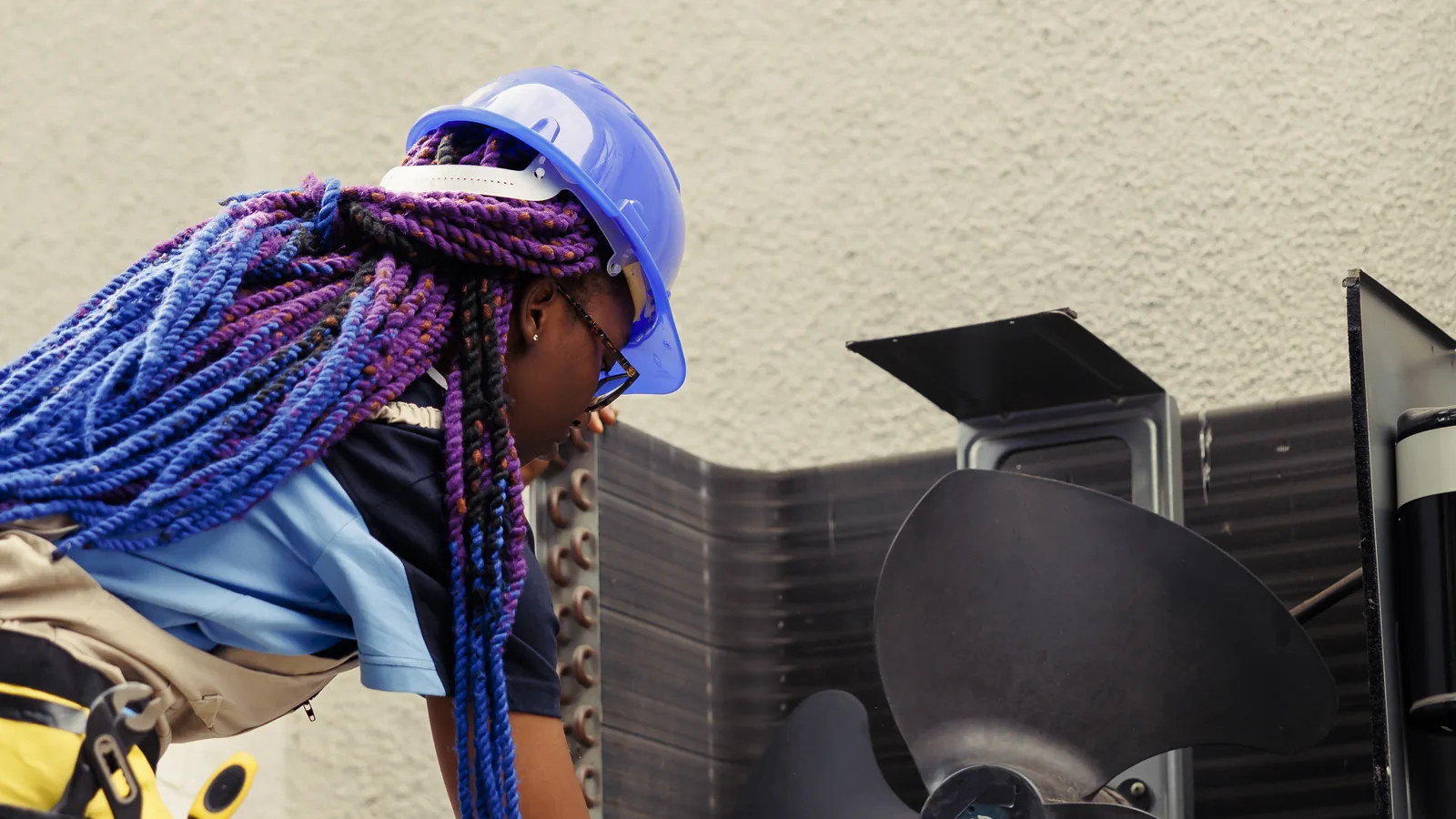 A maintenance worker clearing debris from around an outdoor HVAC unit